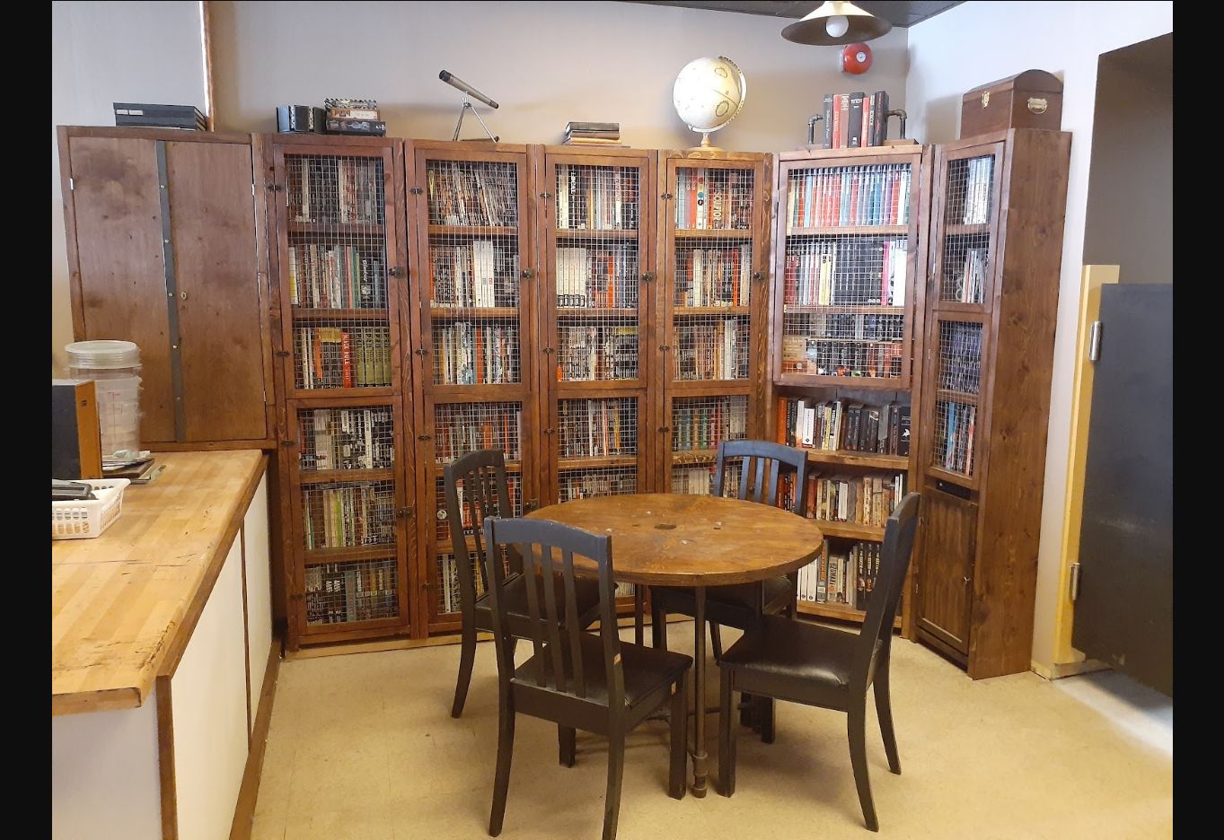 Round wooden table and dark chairs in front of book-filled wooden cabinets with wire-mesh doors.